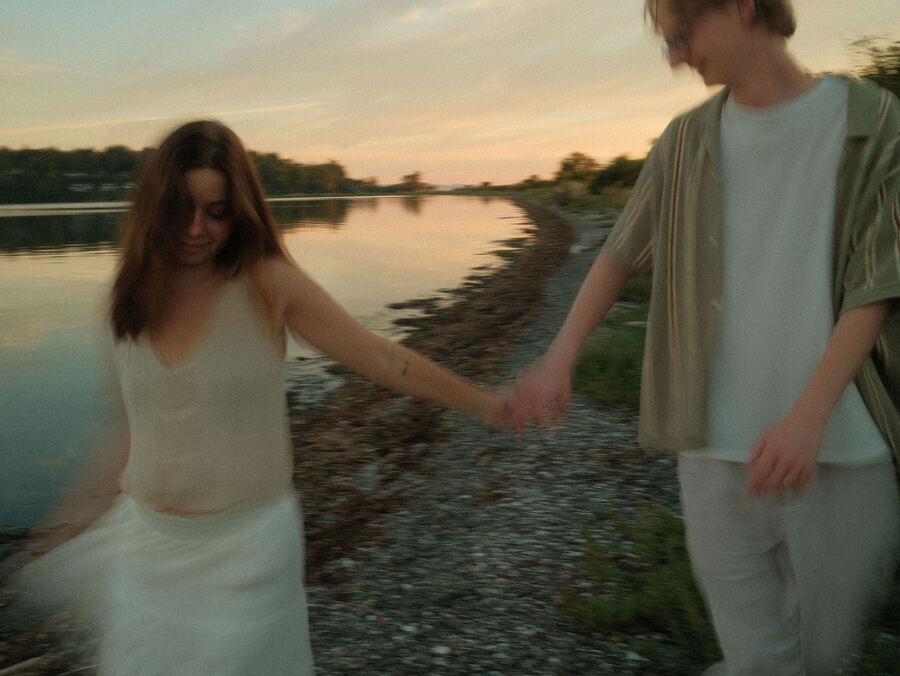 Couple holding hands by a calm river at dusk