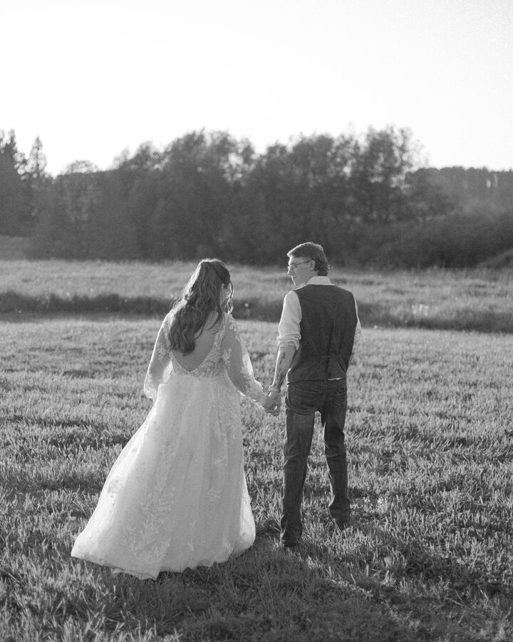 Black and white couple holding hands as they walk through a sunlit field